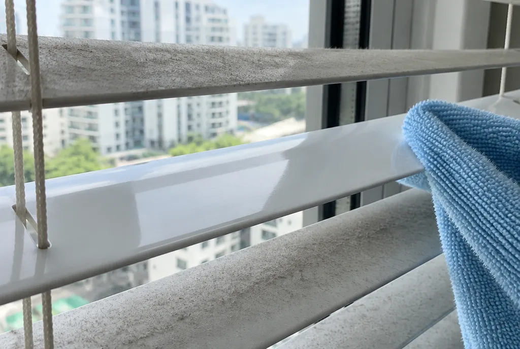 Dust being wiped off an aluminium venetian blind slat.